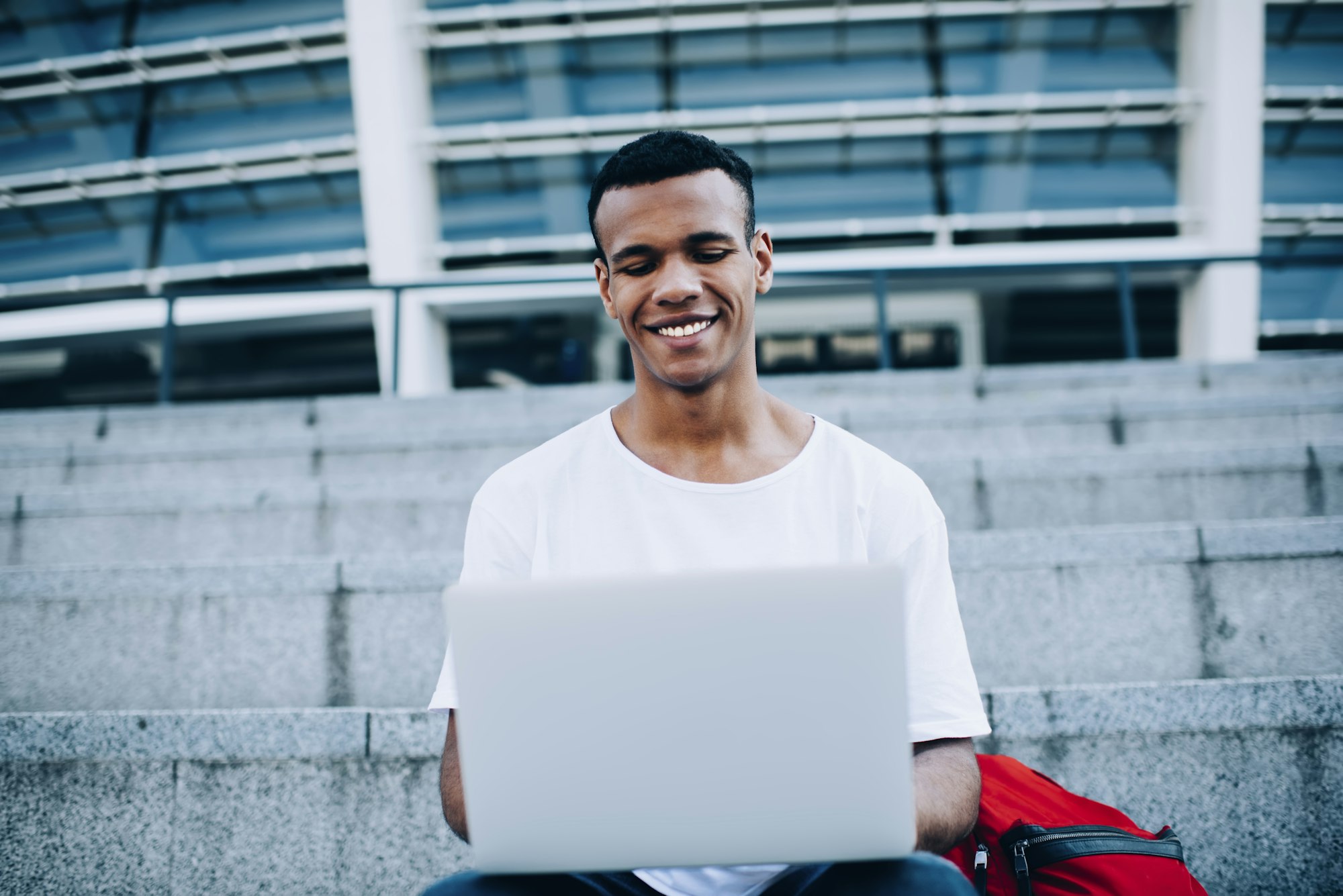 Cheerful black guy with laptop on steps